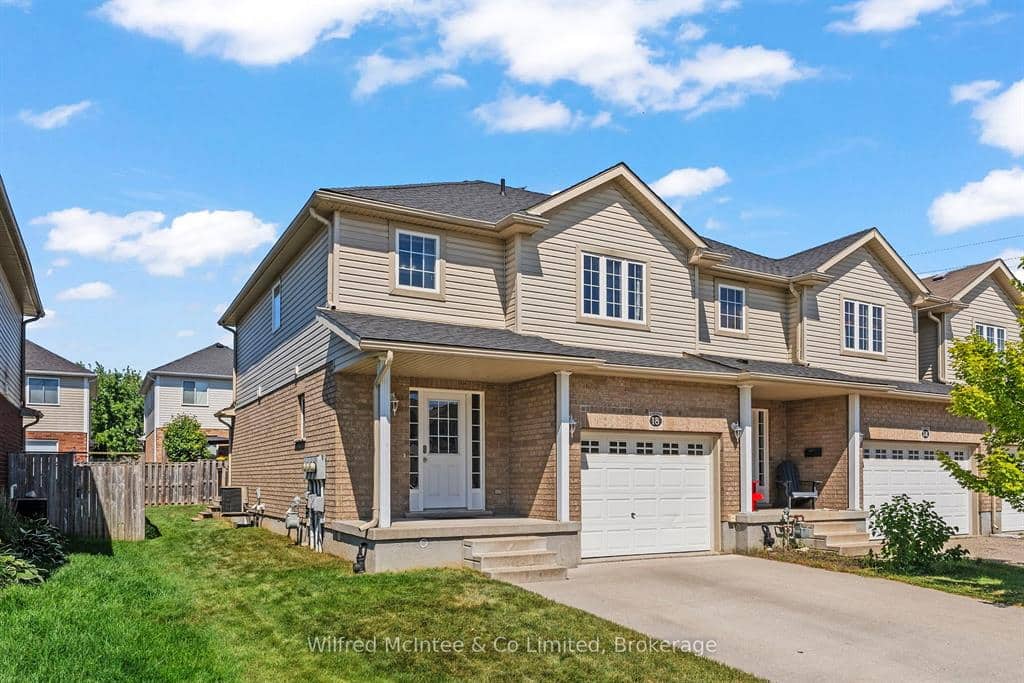 A two-story semi-detached house with beige siding, a single-car garage, and a covered front porch on a sunny day.