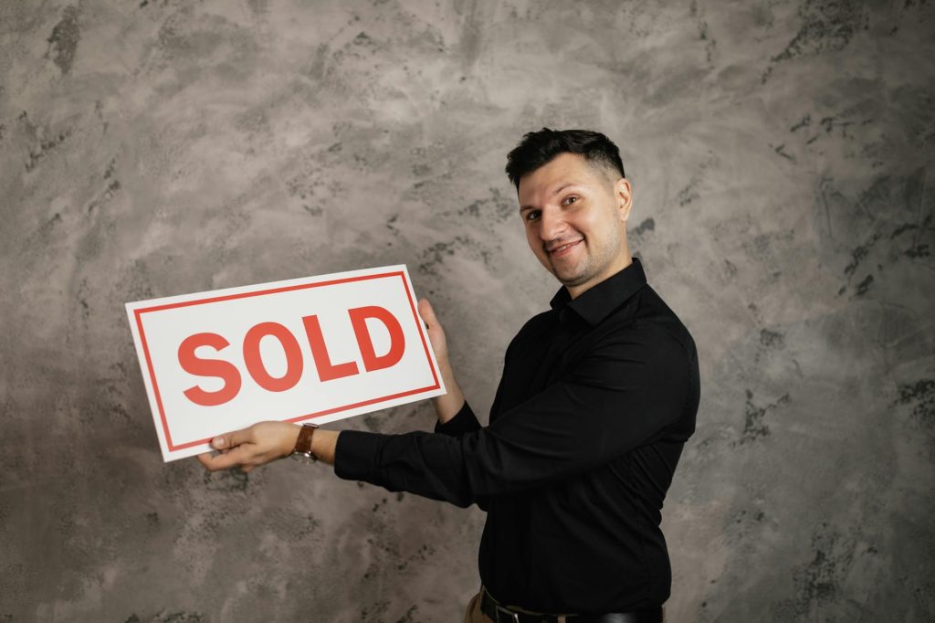 Happy realtor holding a 'Sold' sign, symbolizing successful property sale.