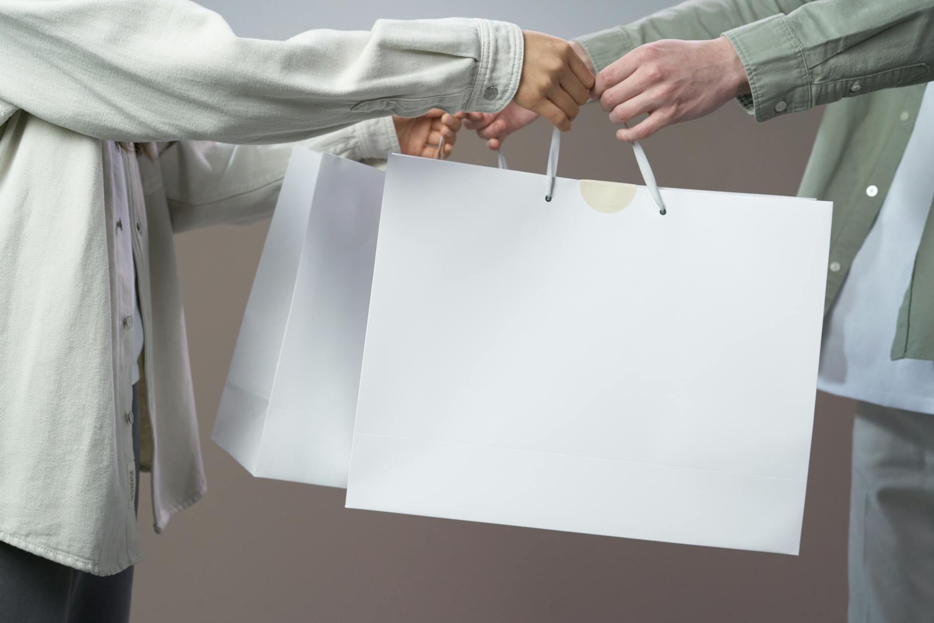 Midsection view of two people exchanging white shopping bags indoors.