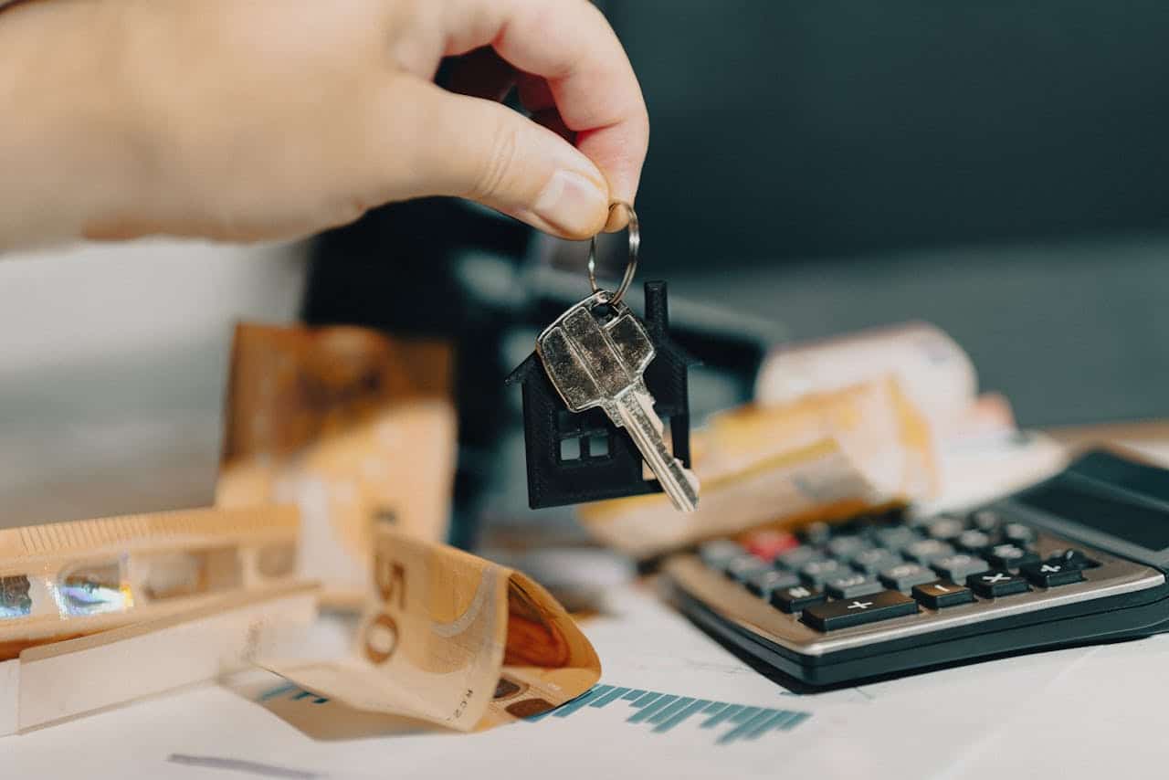 A hand holds house keys over a table with euro banknotes, a calculator, and financial documents.