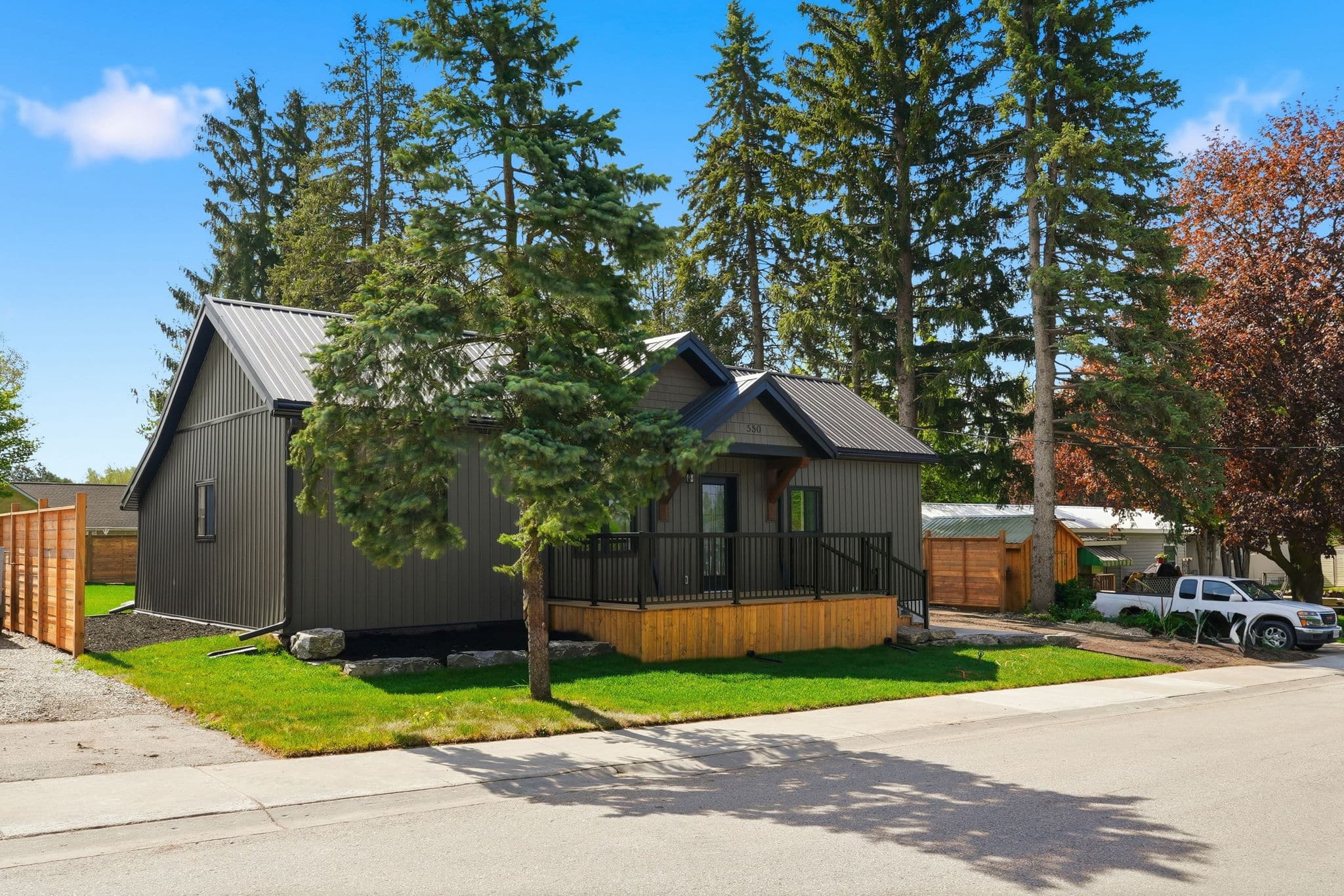 Single-story, dark gray house with a covered front porch, surrounded by trees and grass, on a suburban street with a white car parked nearby.