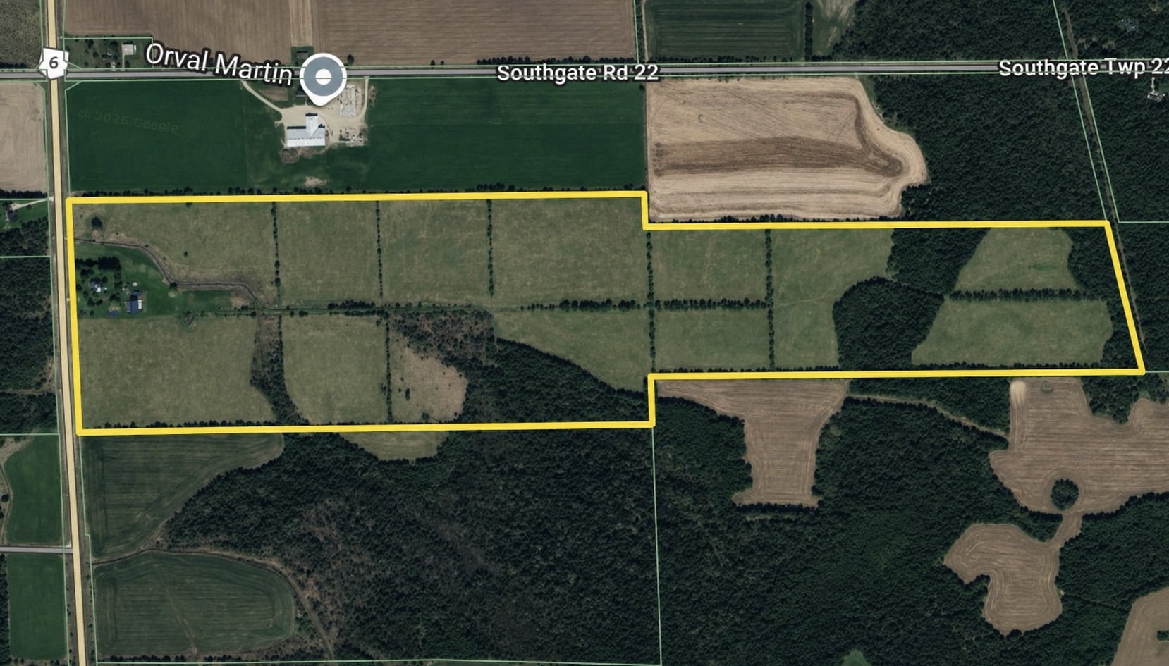 Aerial view of a rectangular plot of farmland outlined in yellow, surrounded by fields, forest, and intersecting roads.
