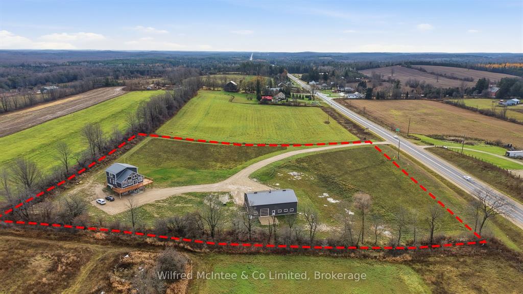 Aerial view of a rural property outlined in red, featuring a house, a barn, a driveway, open grass areas, and a road running alongside the property.